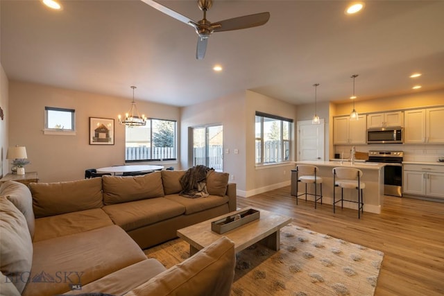 living area with light wood finished floors, recessed lighting, ceiling fan with notable chandelier, and baseboards