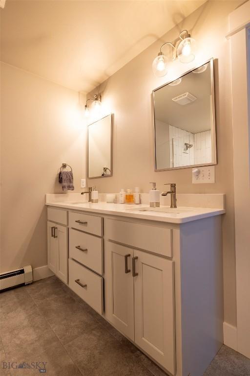 full bath with double vanity, baseboard heating, baseboards, and a sink