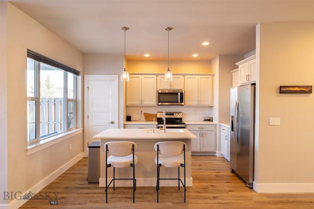 kitchen featuring a kitchen bar, decorative backsplash, light wood-style flooring, appliances with stainless steel finishes, and a kitchen island with sink