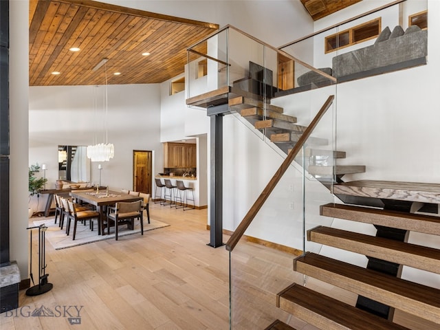 staircase with an inviting chandelier, wooden ceiling, a high ceiling, and wood finished floors