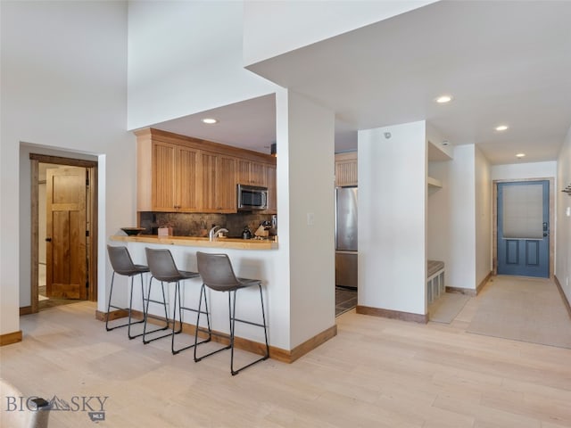 kitchen featuring light wood-style flooring, stainless steel appliances, a breakfast bar area, light countertops, and decorative backsplash