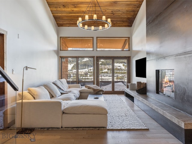 living area with wood finished floors, a high ceiling, wood ceiling, a glass covered fireplace, and a notable chandelier