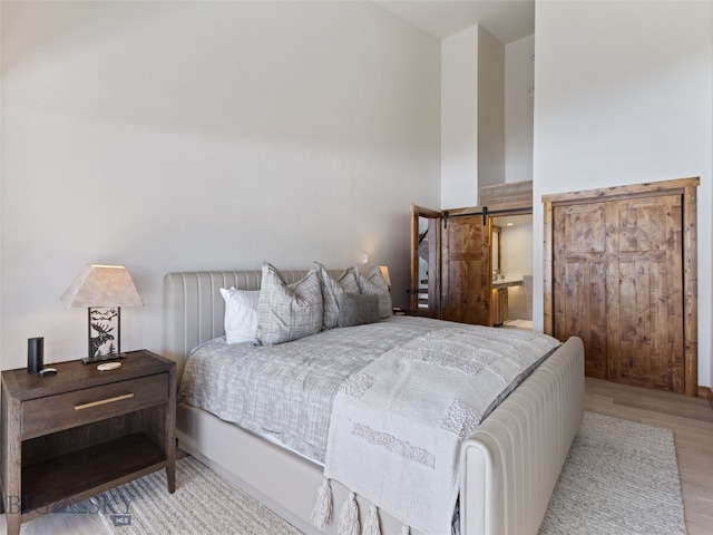 bedroom featuring a barn door, a high ceiling, and wood finished floors