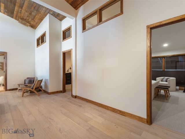 corridor with baseboards, light wood-style flooring, and a towering ceiling