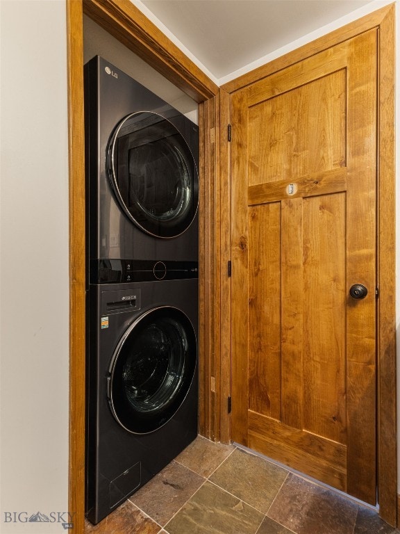 clothes washing area with laundry area, stacked washer and dryer, and stone finish floor