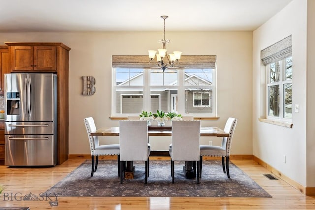 dining space featuring light wood finished floors, visible vents, baseboards, and a notable chandelier