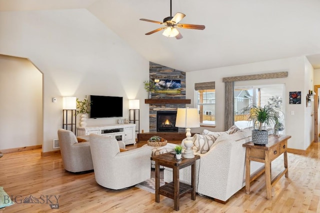 living room with visible vents, ceiling fan, a stone fireplace, light wood-style floors, and high vaulted ceiling