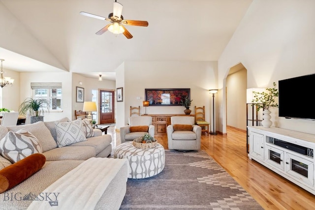 living room with ceiling fan with notable chandelier, high vaulted ceiling, and light wood finished floors