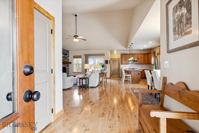 foyer entrance featuring lofted ceiling, light wood-style floors, ceiling fan, and a fireplace