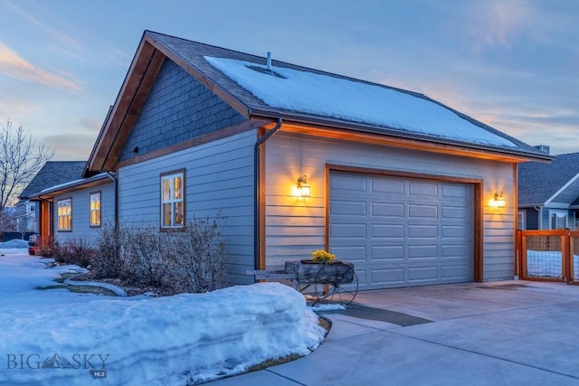 view of snow covered exterior featuring concrete driveway, an attached garage, and a shingled roof