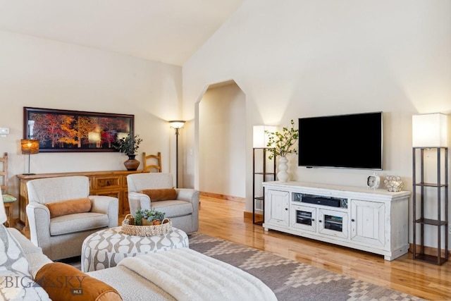 living room featuring light wood-style flooring, baseboards, and high vaulted ceiling