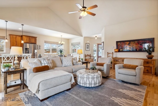 living area with high vaulted ceiling, light wood-style flooring, and ceiling fan with notable chandelier