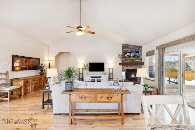 living area with light wood-style flooring, high vaulted ceiling, a large fireplace, and ceiling fan