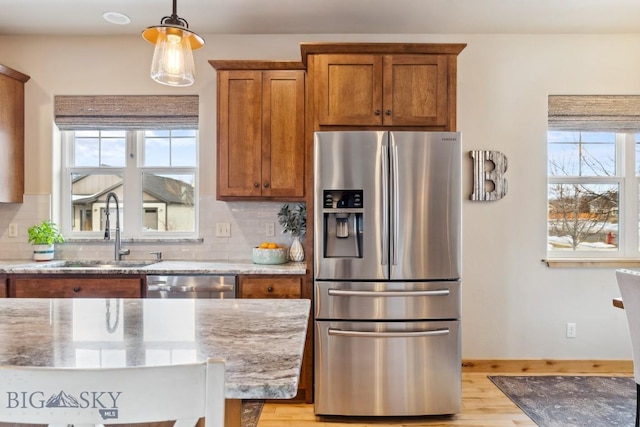 kitchen featuring tasteful backsplash, light stone countertops, brown cabinets, stainless steel appliances, and a sink