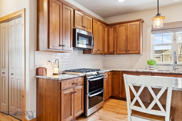 kitchen featuring decorative backsplash, light wood-style floors, brown cabinetry, stainless steel appliances, and a sink