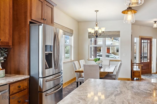 kitchen featuring baseboards, light stone countertops, pendant lighting, brown cabinets, and stainless steel appliances