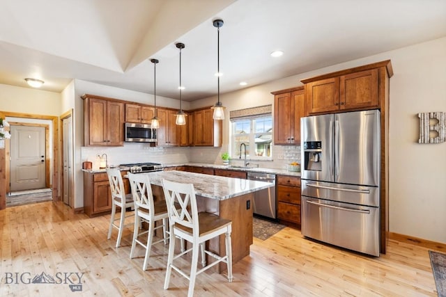 kitchen featuring backsplash, appliances with stainless steel finishes, light wood-style floors, brown cabinetry, and a sink