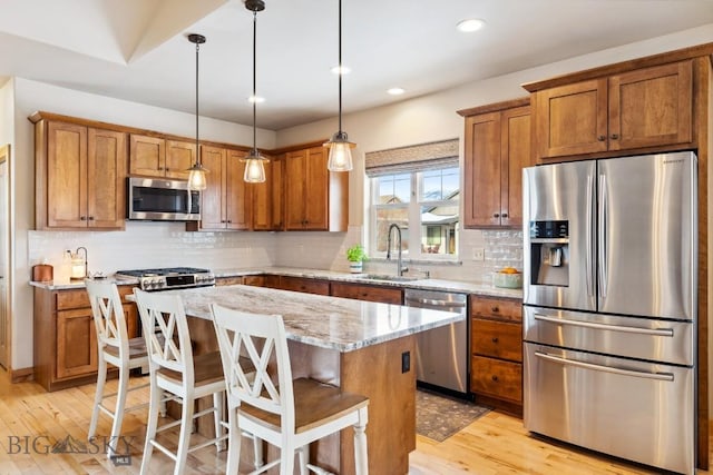 kitchen with a kitchen island, brown cabinets, light wood-style floors, stainless steel appliances, and a sink