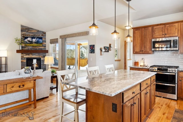 kitchen with light wood-style flooring, a fireplace, vaulted ceiling, appliances with stainless steel finishes, and tasteful backsplash