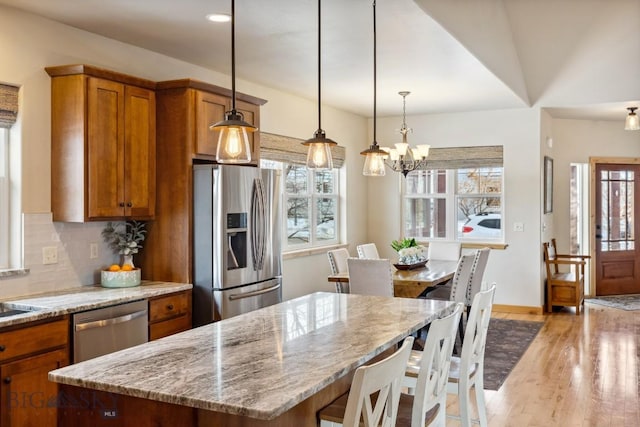 kitchen with light stone countertops, decorative backsplash, light wood-style flooring, brown cabinetry, and stainless steel appliances