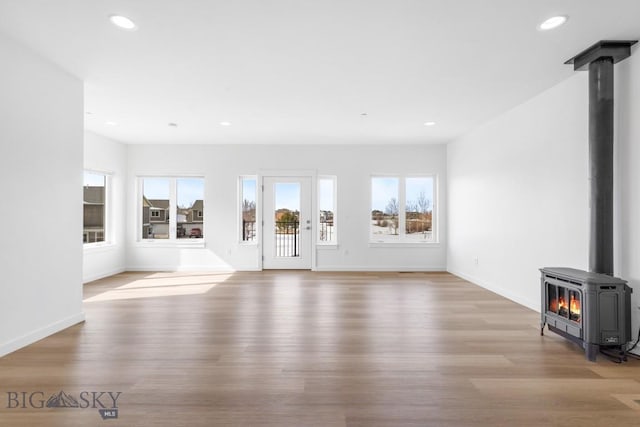 unfurnished living room with a wood stove, recessed lighting, light wood-style floors, and baseboards