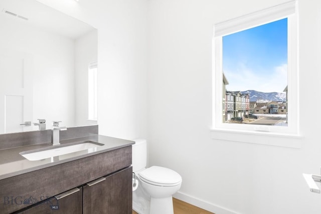 half bath with visible vents, toilet, wood finished floors, baseboards, and vanity