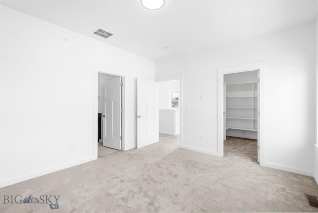 unfurnished bedroom featuring a walk in closet, visible vents, a closet, carpet floors, and baseboards