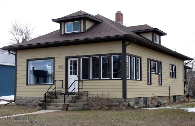 view of front facade featuring a front yard, roof with shingles, and a chimney