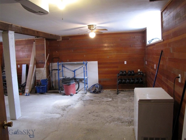 interior space featuring ceiling fan, unfinished concrete flooring, and wood walls