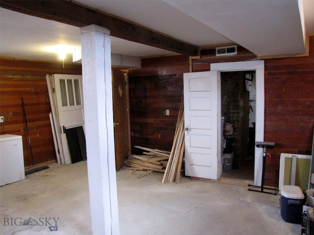 finished below grade area with visible vents, wood walls, and refrigerator