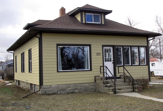 bungalow with entry steps, a chimney, and a shingled roof