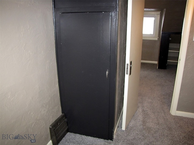 corridor featuring a textured wall, visible vents, carpet floors, and baseboards