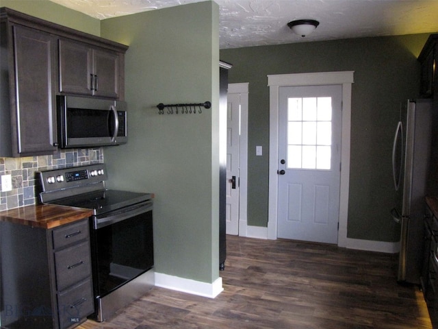 kitchen featuring baseboards, stainless steel appliances, decorative backsplash, dark brown cabinetry, and dark wood-type flooring