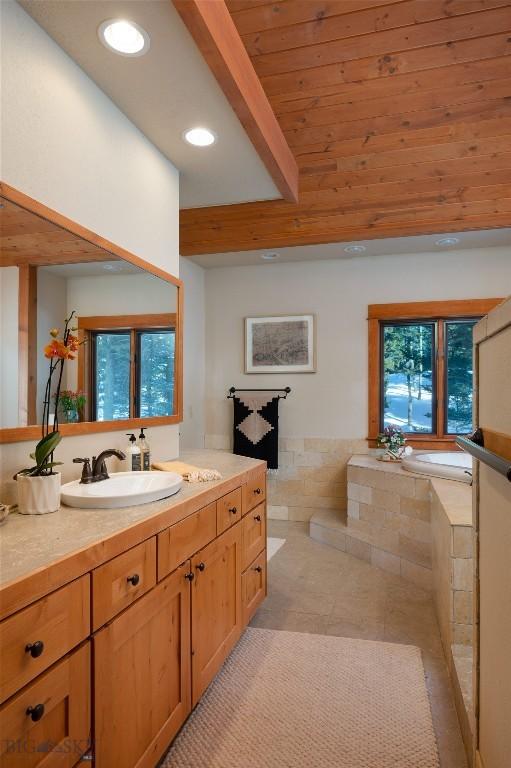 bathroom with tile patterned floors, beamed ceiling, recessed lighting, a relaxing tiled tub, and vanity