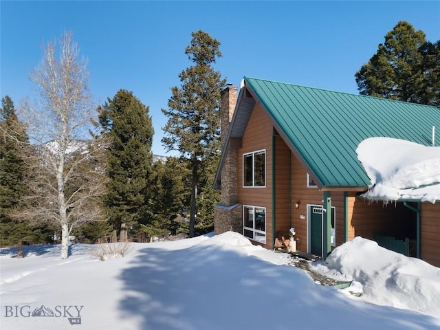 snow covered property with metal roof, a chimney, and a standing seam roof