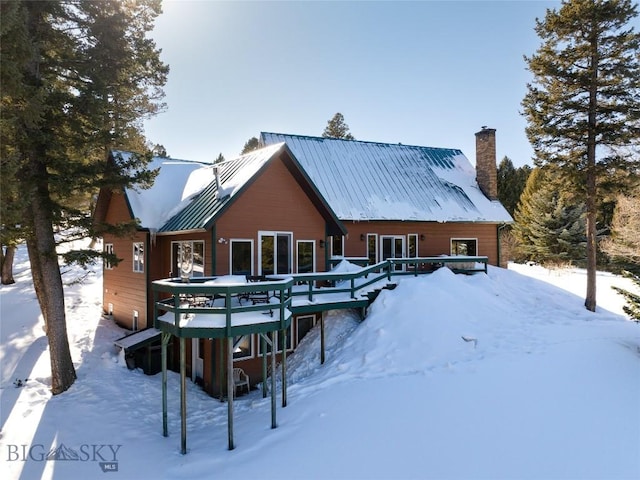 snow covered house featuring a wooden deck and metal roof