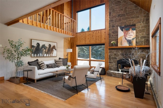 living area featuring visible vents, wood walls, hardwood / wood-style floors, a stone fireplace, and high vaulted ceiling