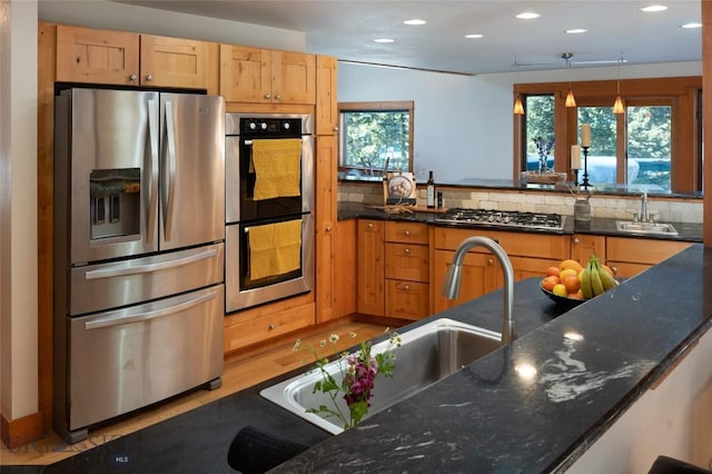 kitchen featuring a sink, dark stone counters, appliances with stainless steel finishes, and pendant lighting