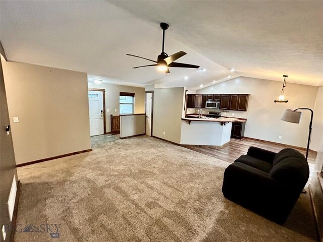 unfurnished living room with lofted ceiling, baseboards, and light carpet