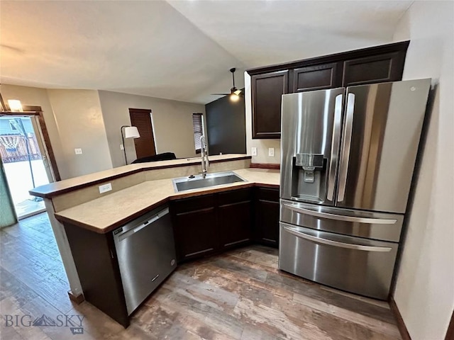 kitchen with a sink, appliances with stainless steel finishes, a peninsula, light countertops, and lofted ceiling