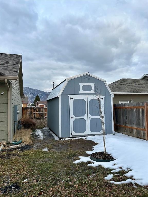 snow covered structure with a mountain view, a storage shed, an outdoor structure, and fence