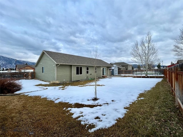 snow covered property featuring an outbuilding, a trampoline, a fenced backyard, and a yard