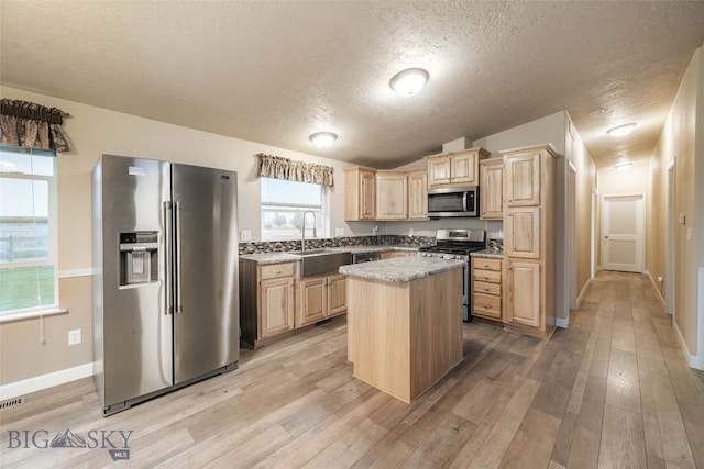 18287 Haasakker Rd, Three Forks, MT 59752 - kitchen with appliances with stainless steel finishes, light brown cabinetry, a textured ceiling, light wood finished floors, and a center island