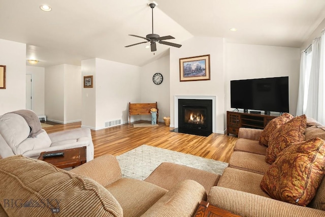 living room with visible vents, a fireplace with flush hearth, light wood-style flooring, recessed lighting, and vaulted ceiling