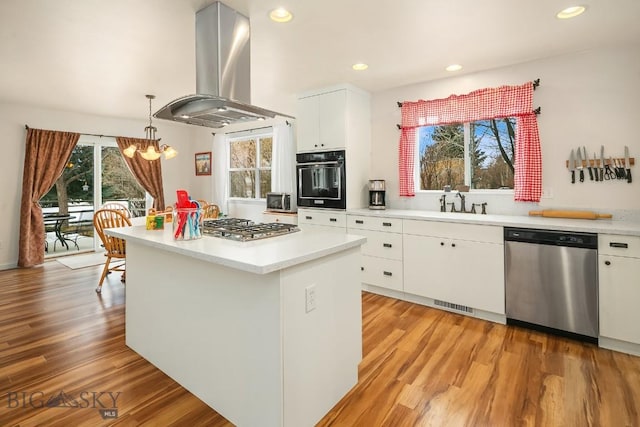 kitchen with light wood-type flooring, appliances with stainless steel finishes, white cabinets, island range hood, and light countertops