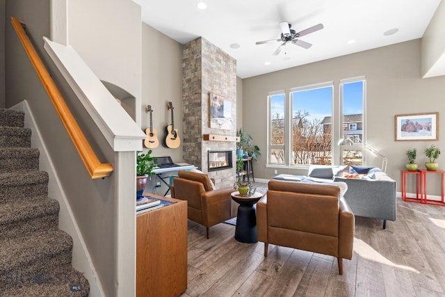 sitting room with light wood finished floors, a fireplace, stairs, and ceiling fan