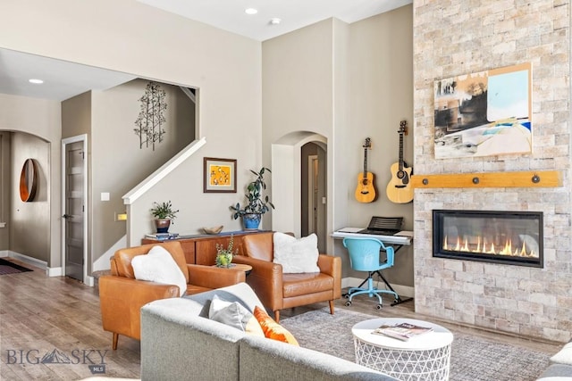 living area with baseboards, stairs, a stone fireplace, wood finished floors, and arched walkways