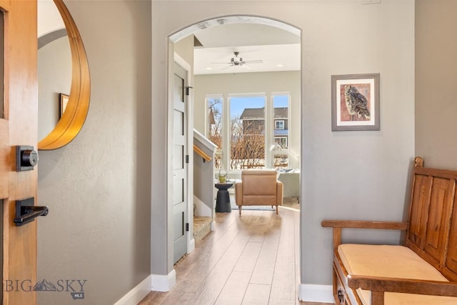 corridor with arched walkways, stairs, light wood-type flooring, and baseboards