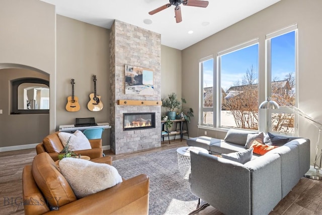 living area with ceiling fan, baseboards, a stone fireplace, and wood finished floors