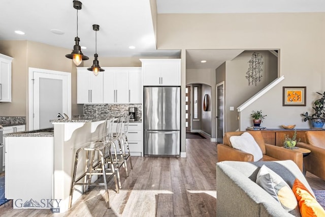 kitchen with a breakfast bar area, dark stone countertops, freestanding refrigerator, light wood-style floors, and arched walkways